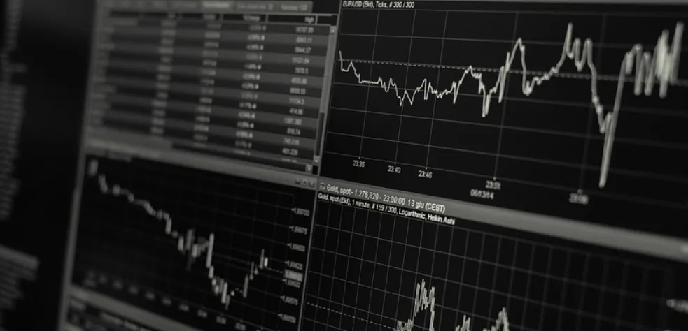 Black-and-white photo of monitors showing line charts and candlestick charts