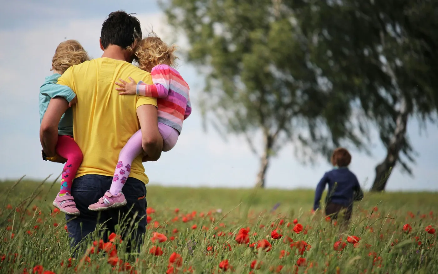Parent carrying two children through a field of flowers